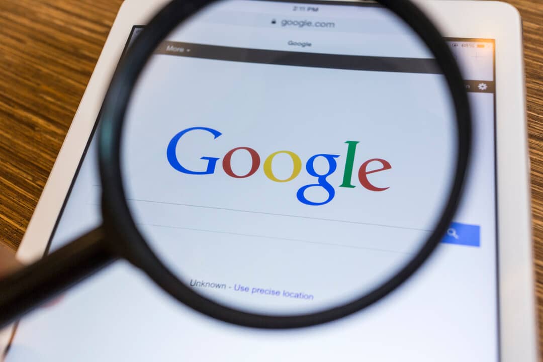 Photo of a phone looking through a magnifying glass at Google's homepage